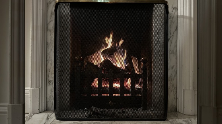 A black mesh fireplace screen in front of a modern marble fireplace.