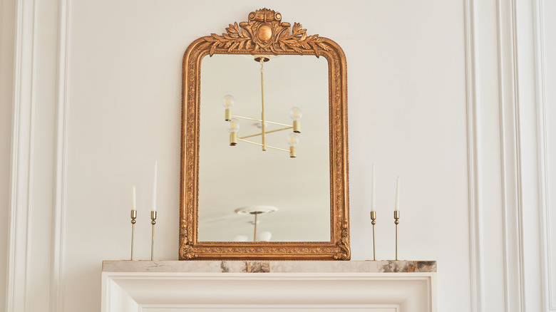 An oversized gold mirror and gold tapered candlesticks sitting on a fireplace mantel.