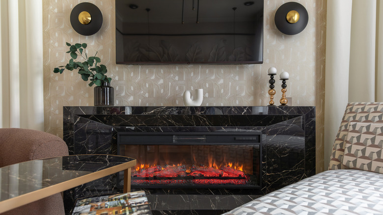 A modern, black marble fireplace with a geometric feature wall covered in wall paper sitting behind it.