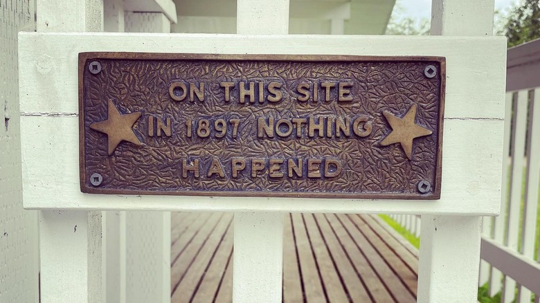 A brown plaque on a white fence declaring nothing important happened in 1897