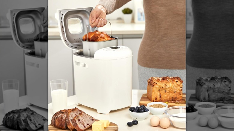 A person pulls a bread loaf out of a bread maker.