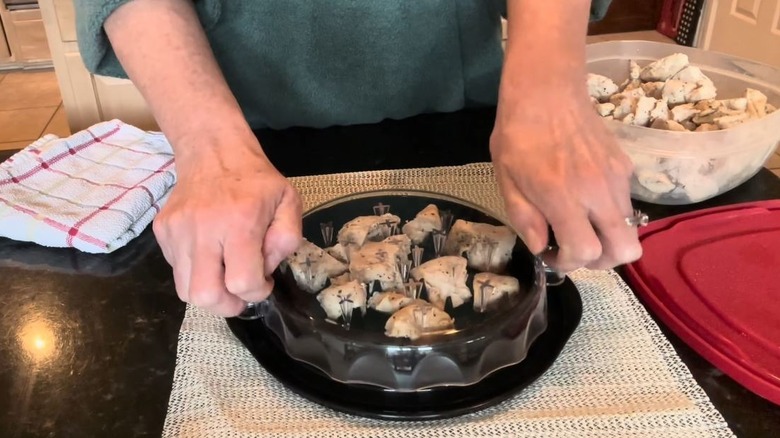 A person holds a chicken shredder with small pieces of chicken inside.