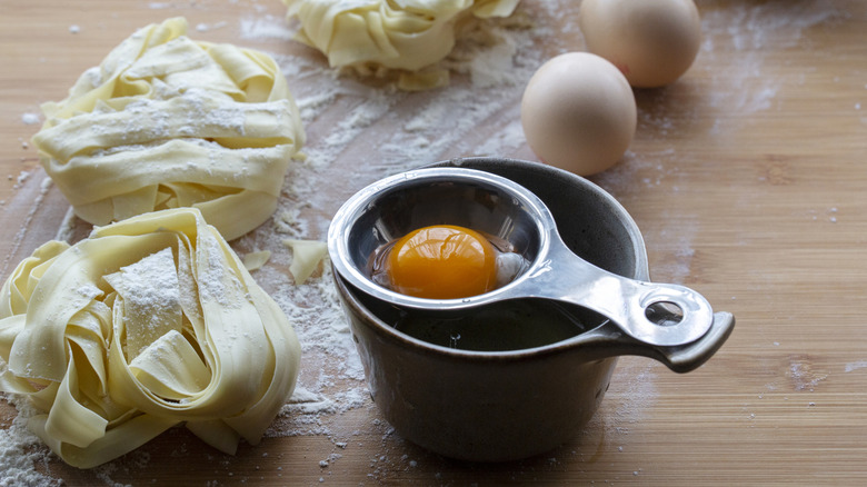 An egg separator holding the yolk as the white catches in a measuring cup underneath.