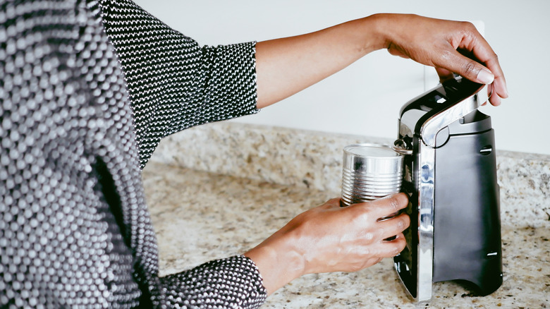 A woman uses a countertop electric can opener.