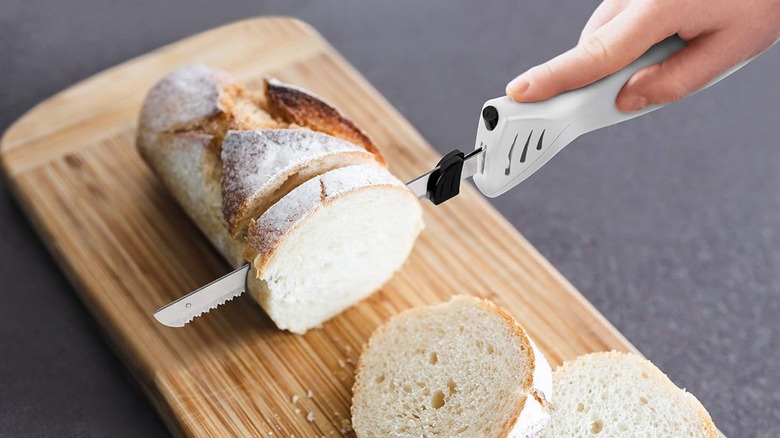 A person cuts bread with an electric knife.