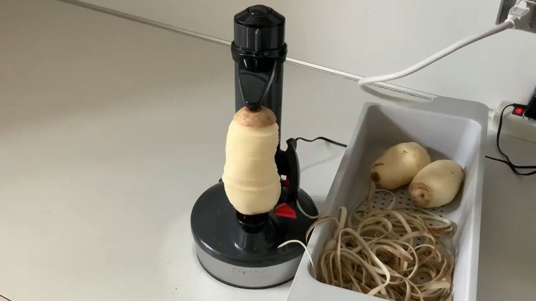 A person prepares thin french fries as an electric potato peeler peels a potato.