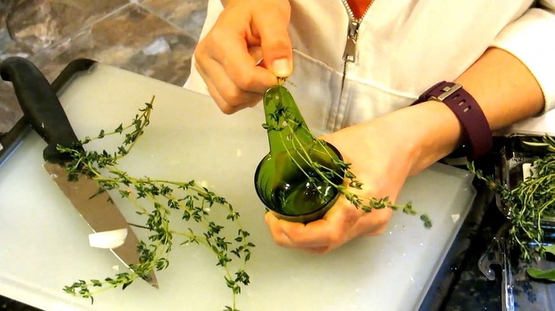 A person pulls herbs through an herb stripper over a chopping board.
