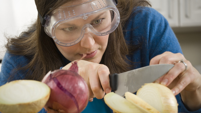 A woman cuts an onion wearing onion goggles.