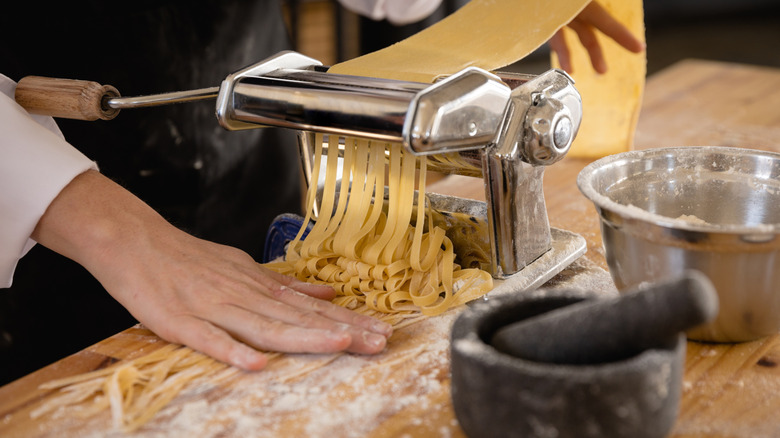 A person runs pasta dough through a pasta machine.