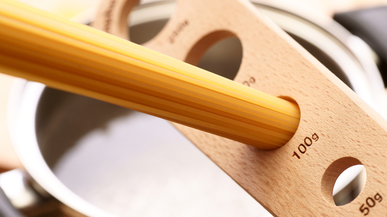 Dry pasta slotted through a pasta measurer with a pan of water in the background.
