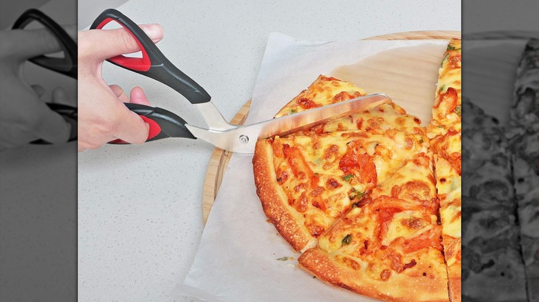 A person cuts pizza slices using pizza scissors.