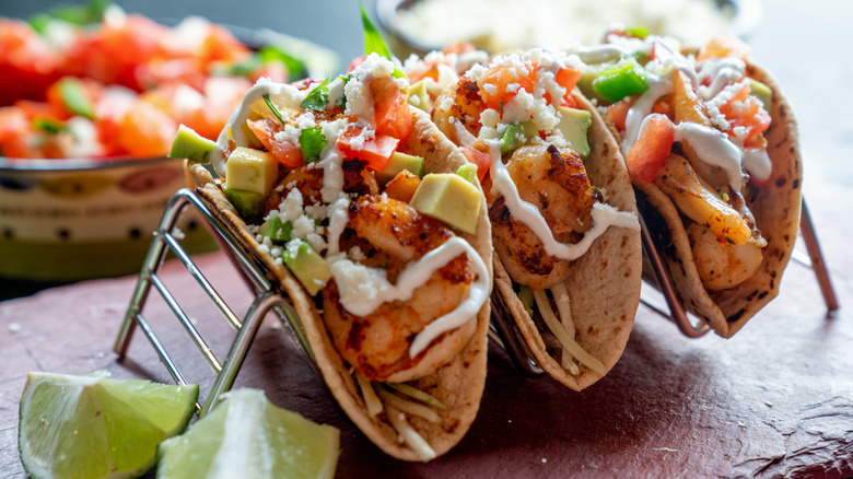 Three tacos rest in a metal taco holder.