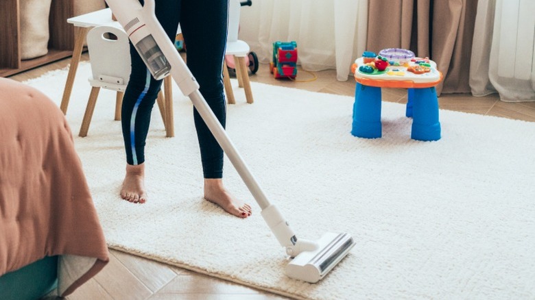 A person vacuuming a child's play room with a cordless stick vacuum.