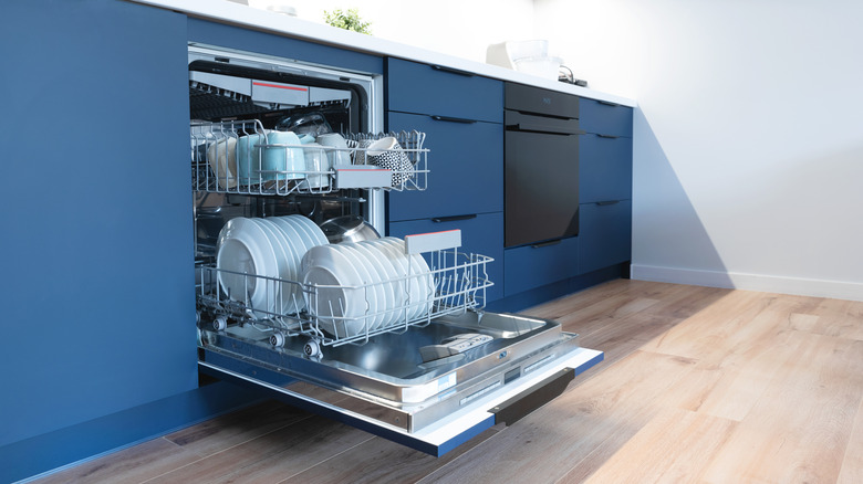 An open dishwasher full of clean dishes in a royal blue kitchen.