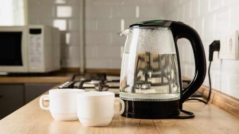 Two coffee cups and a clear electric kettle filled with water on kitchen counter
