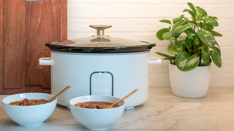 A pale blue slow cooker with two bowls of stew in the same colour in front of it.