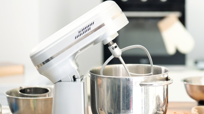 A bright fire engine red stand mixer with whisk and a man cracking an egg into the bowl.