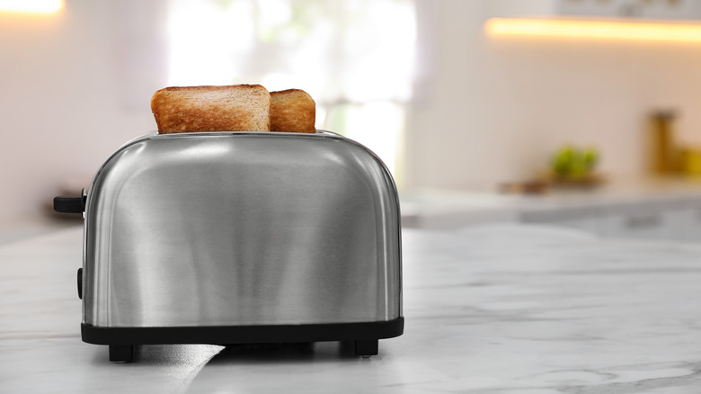 A chrome toaster with two slices of toast in it against a blurred kitchen counter backdrop