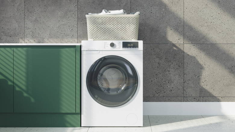 A washing machine next to green cabinets with a laundry basket on top of the machine.