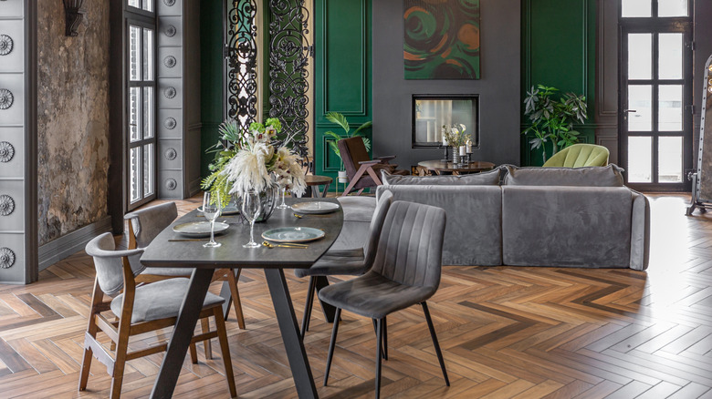 An open living and dining area with metal table, grey sofa and dining room chairs and a metal lattice framwork on one wall.