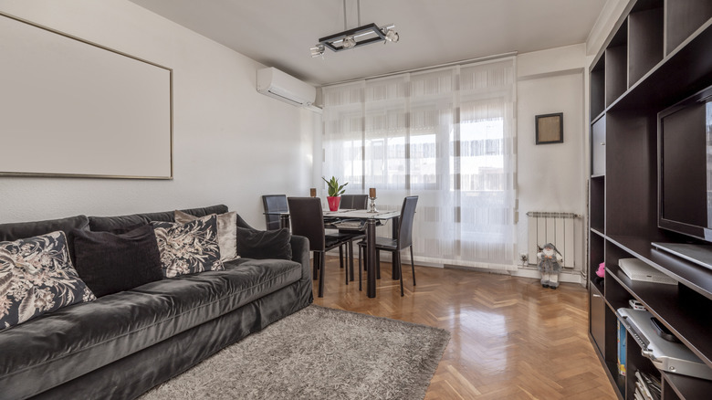 A large dark bookcase opposite a grey velvet sofa and cream wall.