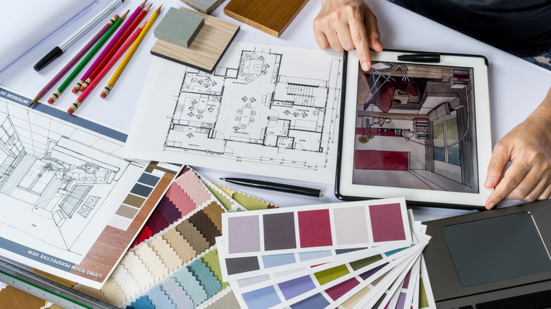 An interior designer works on a project on a table surrounded by swatches and floorplans.
