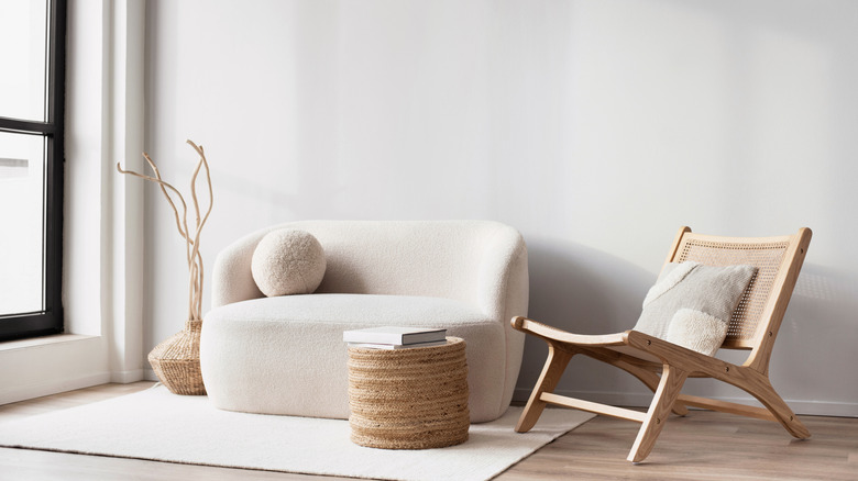 A minimalist living room with a cream couch, a wooden chair, and a woven coffee table.