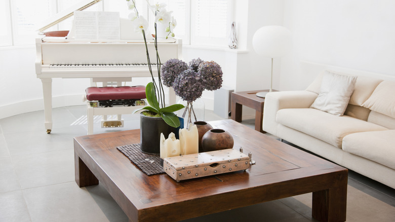 A wooden coffee table with décor items on it in an all-white living room.
