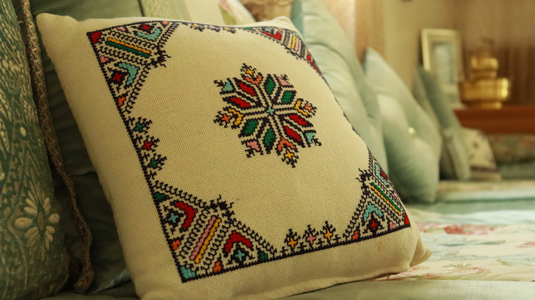 An antique embroidered pillow sitting on a couch.