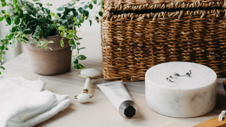A bathroom vanity with a marble container, jade roller, lotion, and other decor pieces.