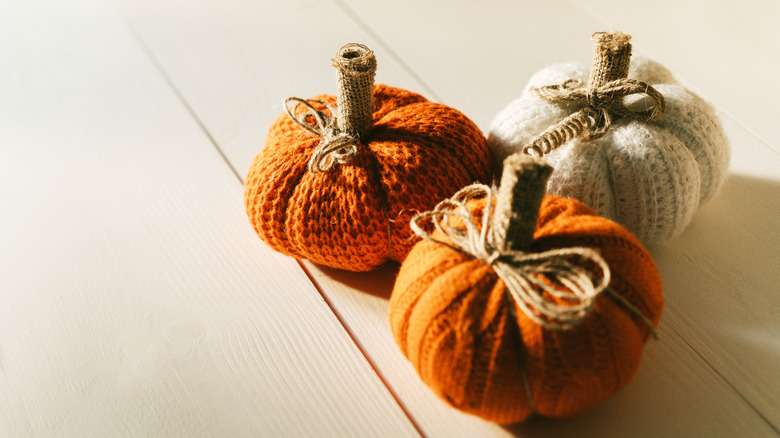 Three fabric pumpkin decoration pieces on white painted floors.