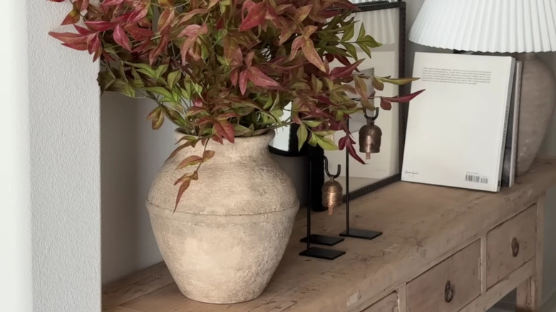 A weathered terracotta vase with fall stems arranged inside.