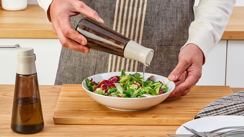 HALVTOM glass and plastic brown bottle with pour spout, pouring oil over salad.