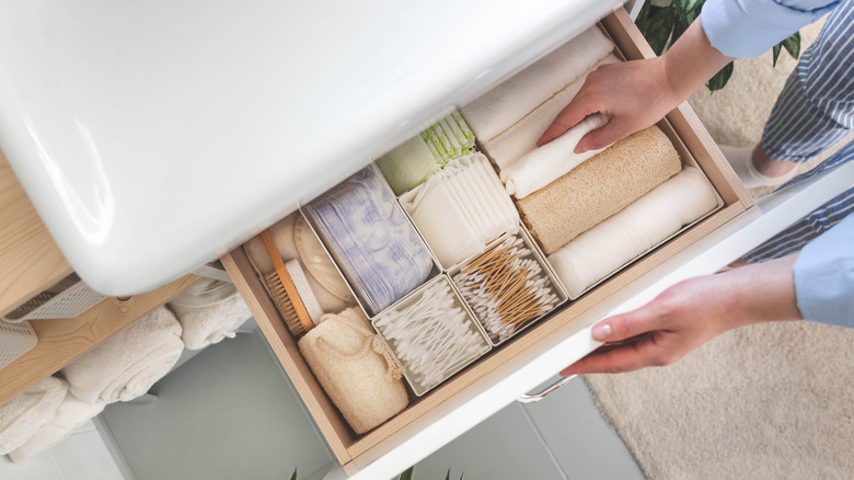Top view of woman hands neatly organizing bathroom amenities and toiletries in drawer or cupboard in bathroom.