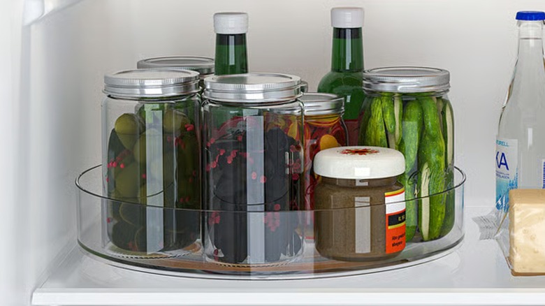 KLIPPKAKTUS plastic lazy susan inside fridge holding containers with pickles and dips.