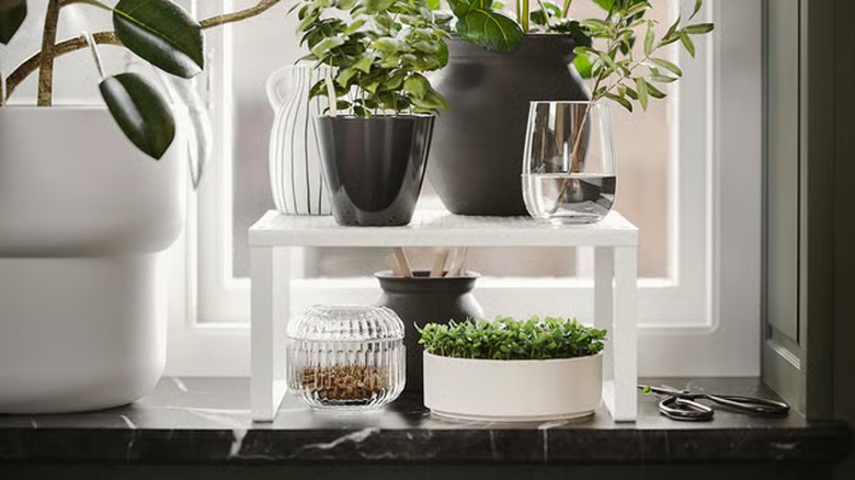 VARIERA shelf insert placed over a marble countertop with small containers underneath and taller vases on top.