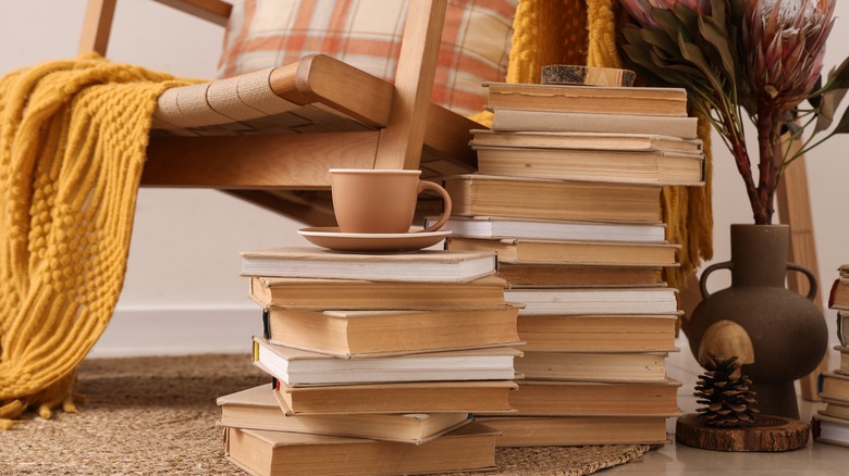 A chair with multiple stacks of books next to it,