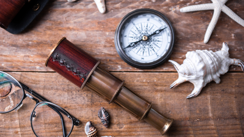 Compass and eye piece next to seashells on table.