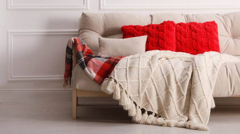Beige couch with red pillows and tartan and wood blanket.