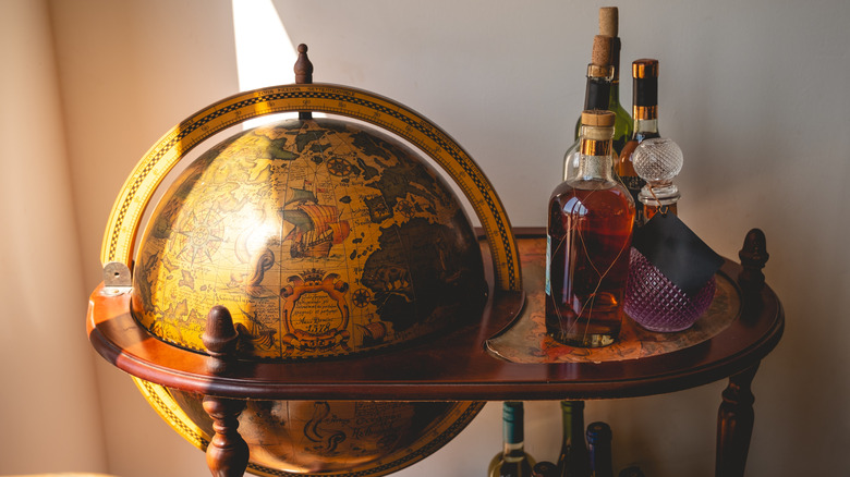 Vintage globe bar cart with alcohol on surface.