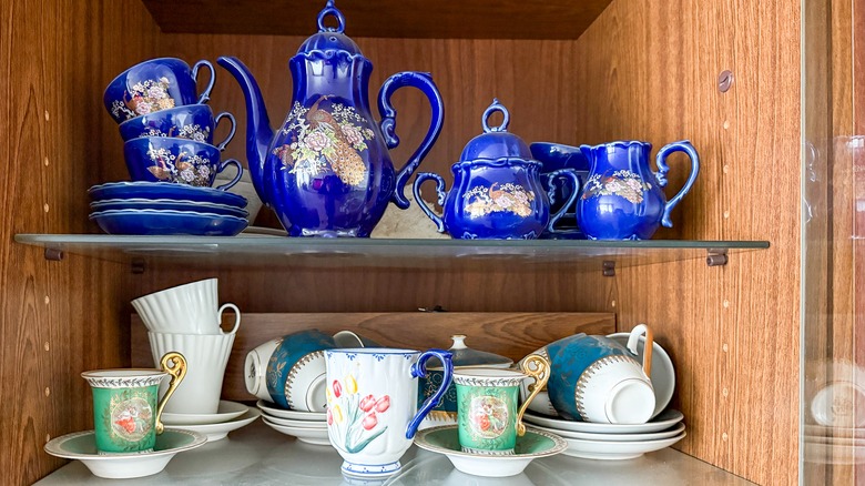 Two sets of tea sets ion glass shelves.