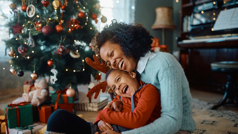 A mom and her son laughing in front of a festive holiday tree