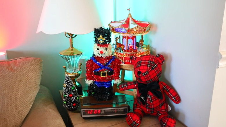 A tinsel toy soldier on top of a vintage clock on a side table.