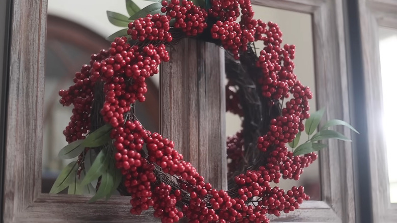 A red berry holiday wreath hanging on a cabinet.