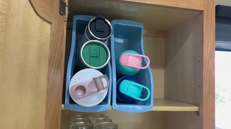 Two blue Dollar Tree book bins in a cupboard with reusable water bottles