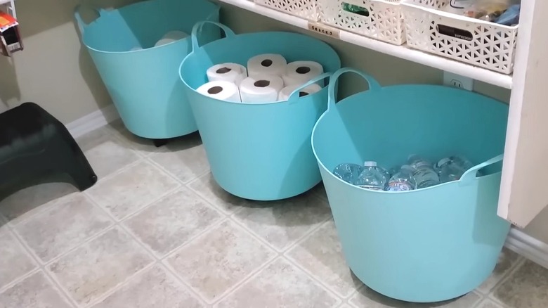 Three large turquoise plastic tubs with rollers on the bottom in the pantry