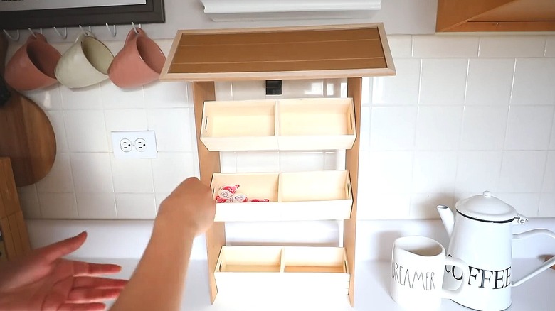 Person filling a DIY wooden crate organizer with coffee items