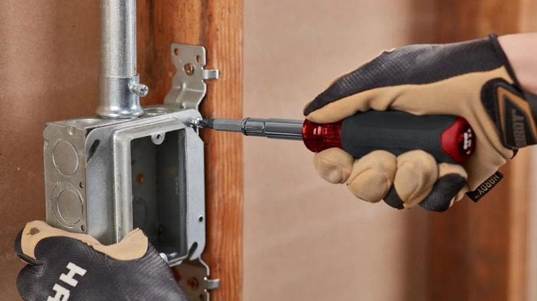 Person using a Doyle screwdriver on a metal electrical junction box