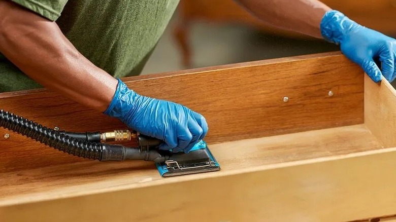 Person using a sander on the inside of a cabinet drawer