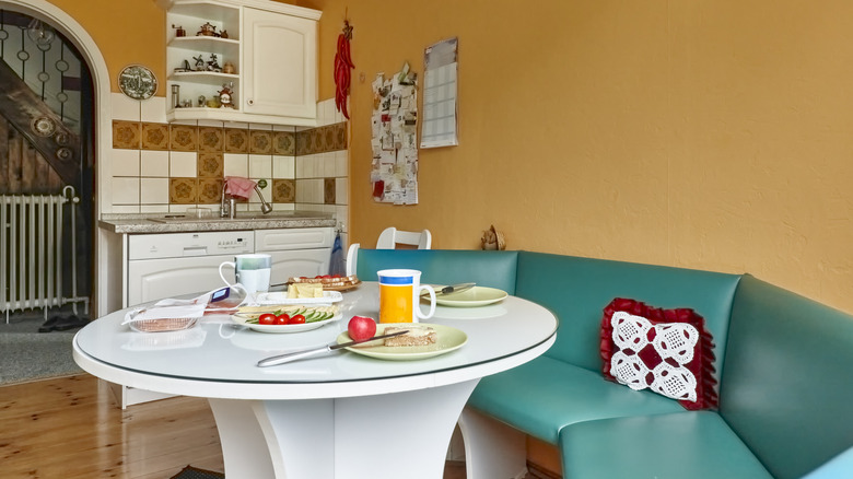 A kitchen with a green breakfast booth and a white dining table.